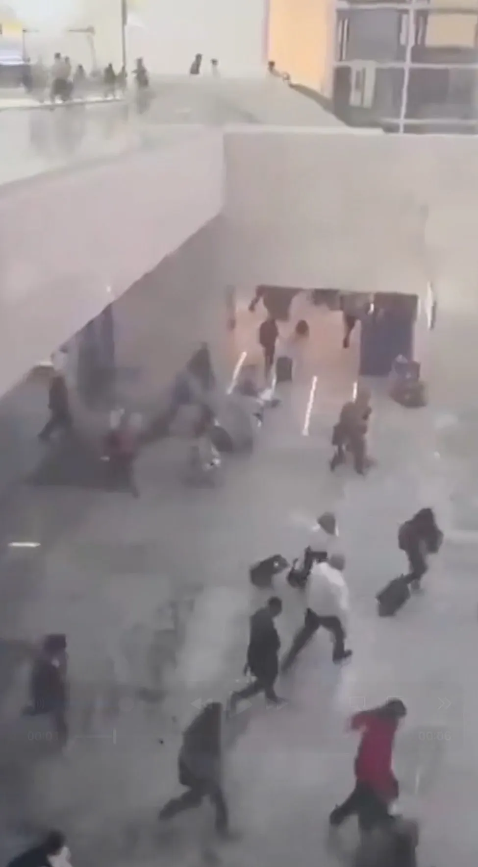 Dozens of people running through an airport terminal away from an unseen threat.