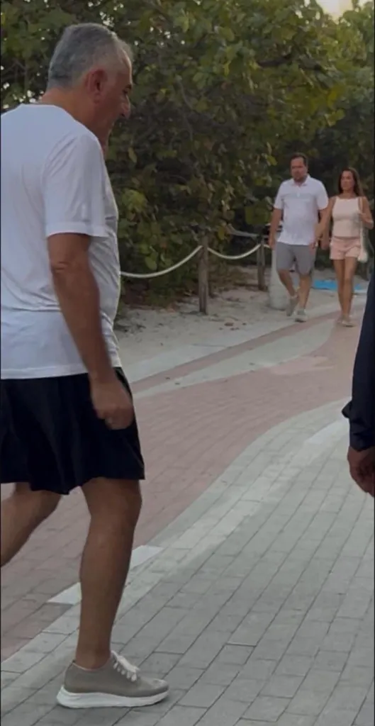 Reza Pahlavi walking outdoors in a white shirt and black shorts.