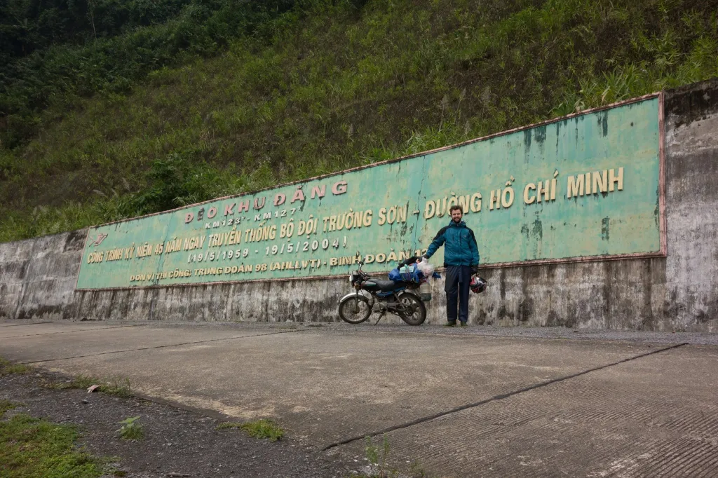 Robert Carroll standing with his motorcycle next to a Ho Chi Minh Trail sign.
