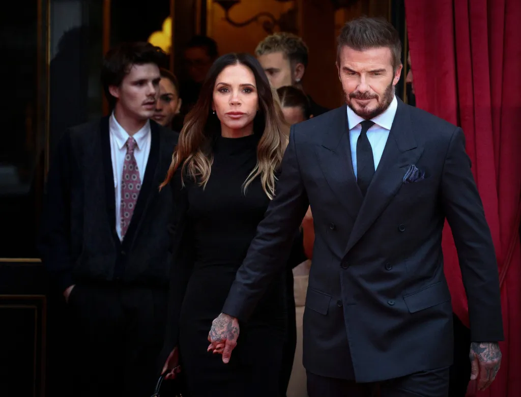 Victoria and David Beckham holding hands, with Cruz and Romeo Beckham walking behind them.