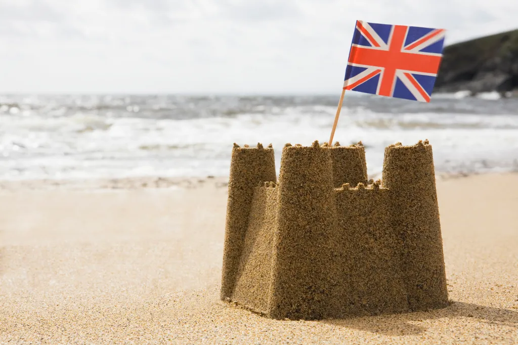 Sandcastle with a Union Jack flag on a sandy beach.