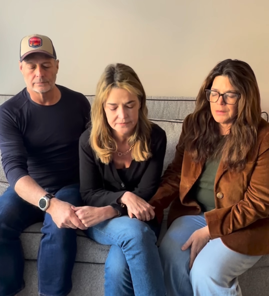 Three individuals, two women and one man, sitting on a couch with their eyes closed and heads bowed, expressing grief.