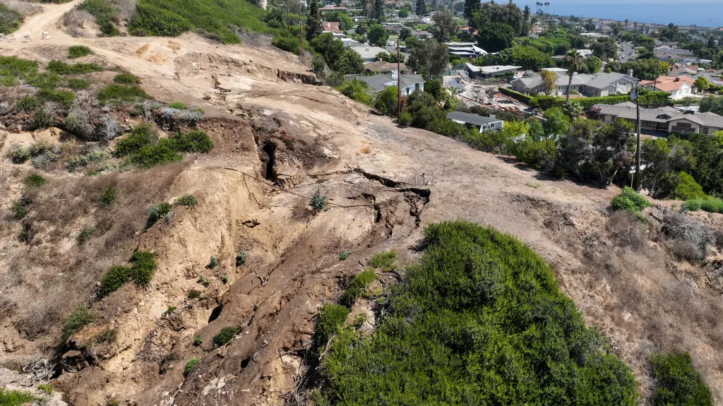 Landslide damage to a hillside in the Seaview neighborhood of Portuguese Bend, with houses visible in the background.