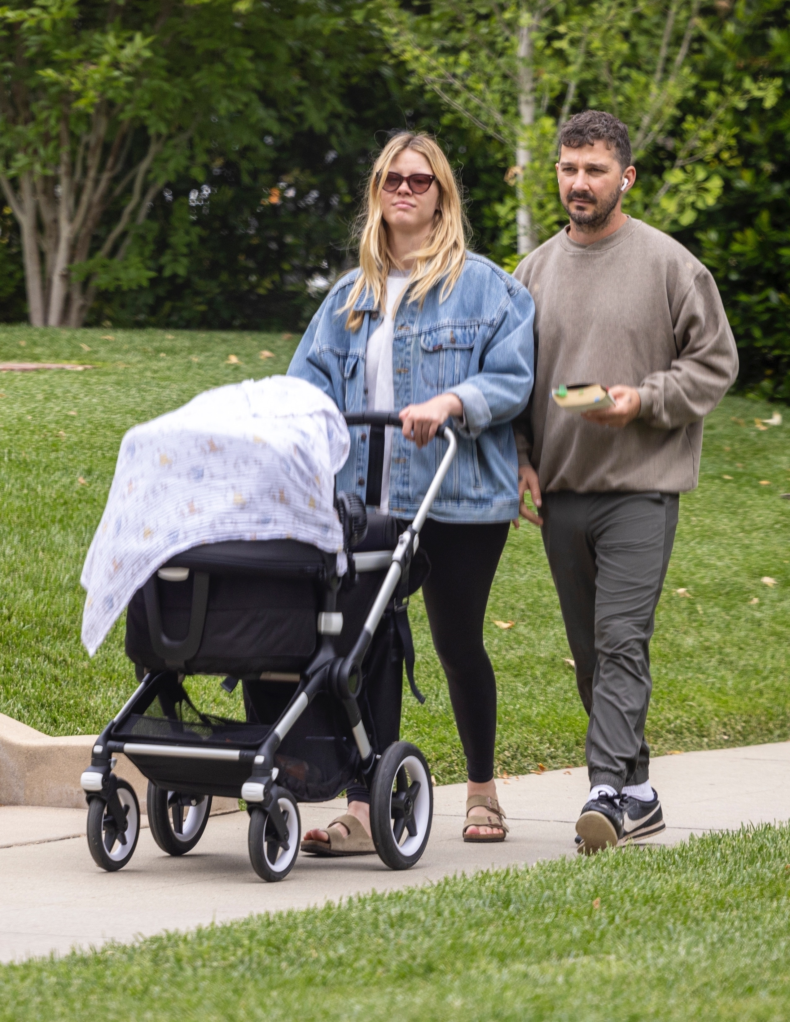 Mia Goth pushes a baby stroller while Shia LaBeouf walks beside her.