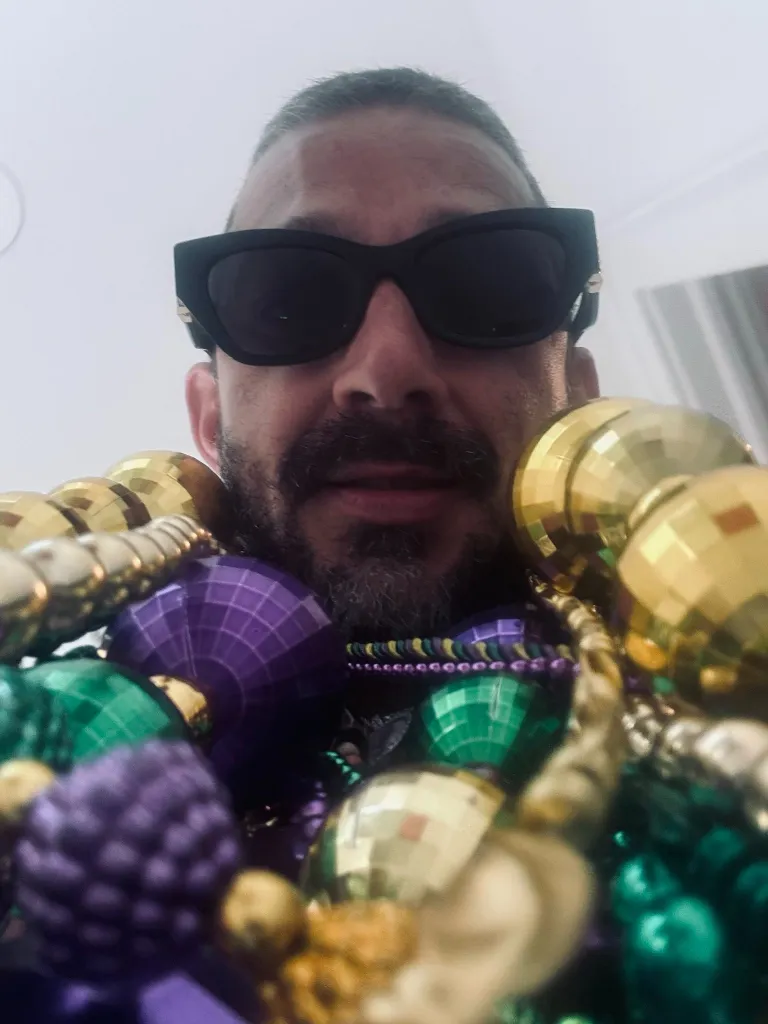 Shia LaBeouf wearing sunglasses and Mardi Gras beads.