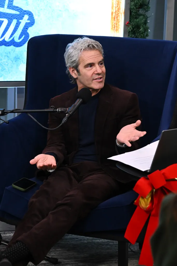 SiriusXM host Andy Cohen sits in a blue chair, speaking into a microphone.
