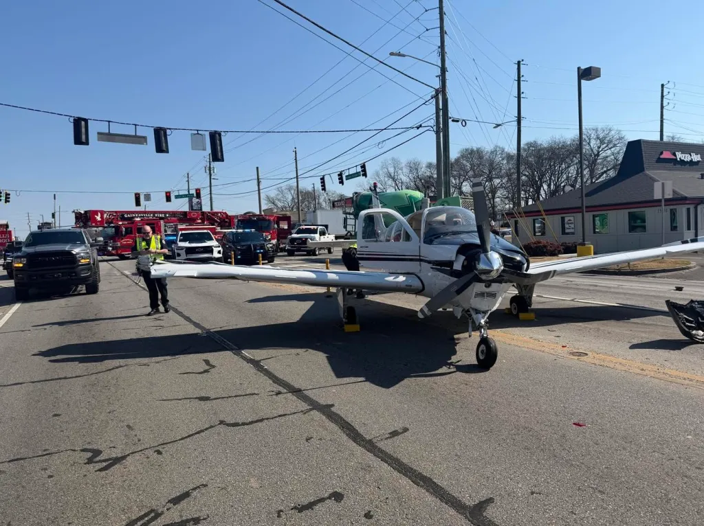 A small plane on a road after an emergency landing, with emergency vehicles in the background.