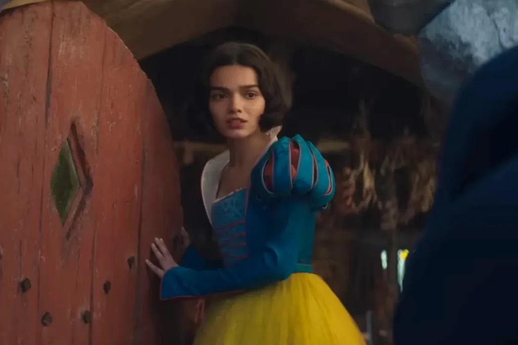 Rachel Zegler as Snow White leaning against a reddish-brown door.