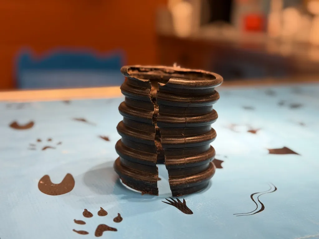 A corrugated pipe, cut open, rests on a blue surface with paw prints.
