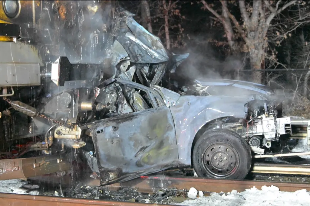 A car severely damaged by a train collision on a railway track.