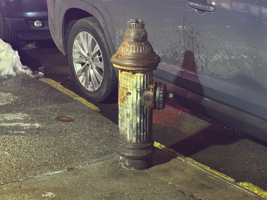 A parked car blocks a fire hydrant on a city street.