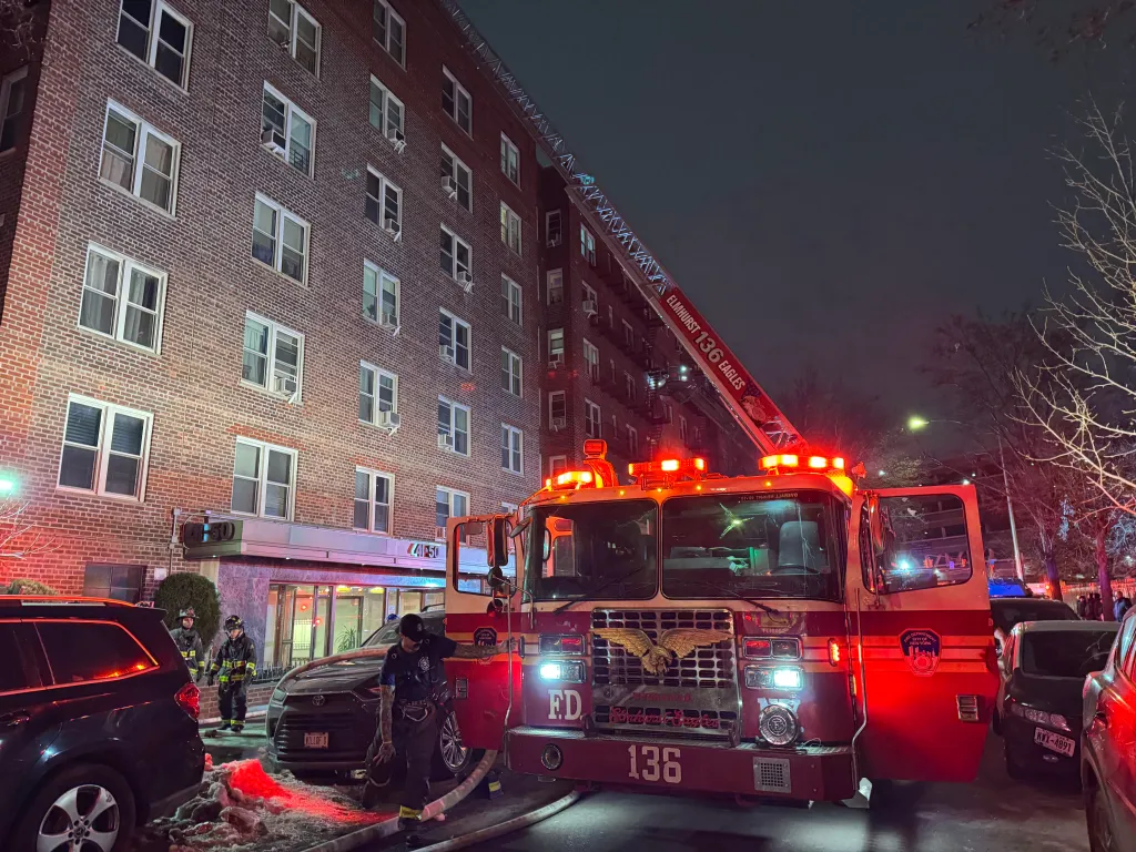 A fire truck with an extended ladder fighting a fire in a building in Queens, New York.