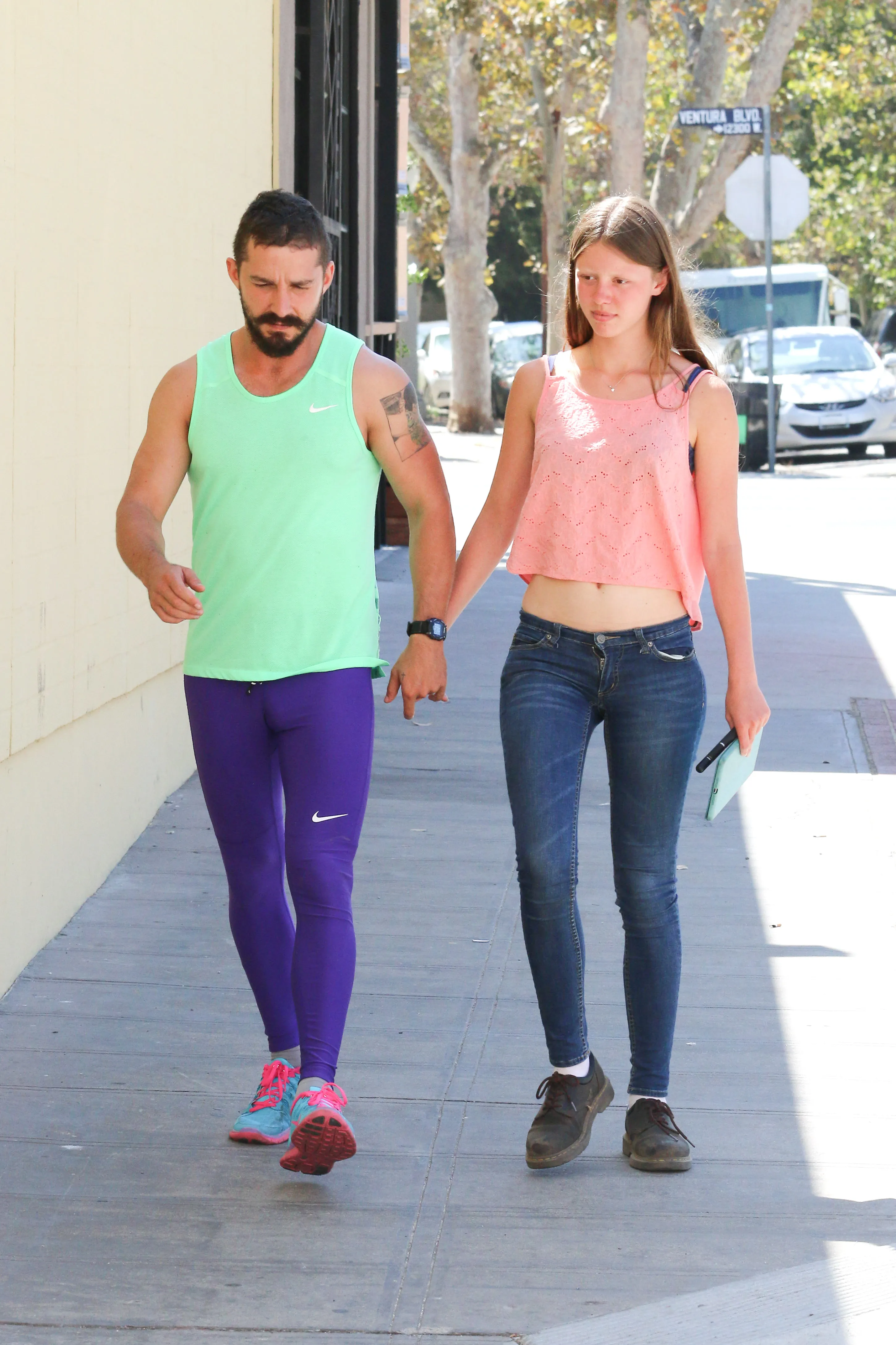 Shia LaBeouf and Mia Goth holding hands while walking outdoors.