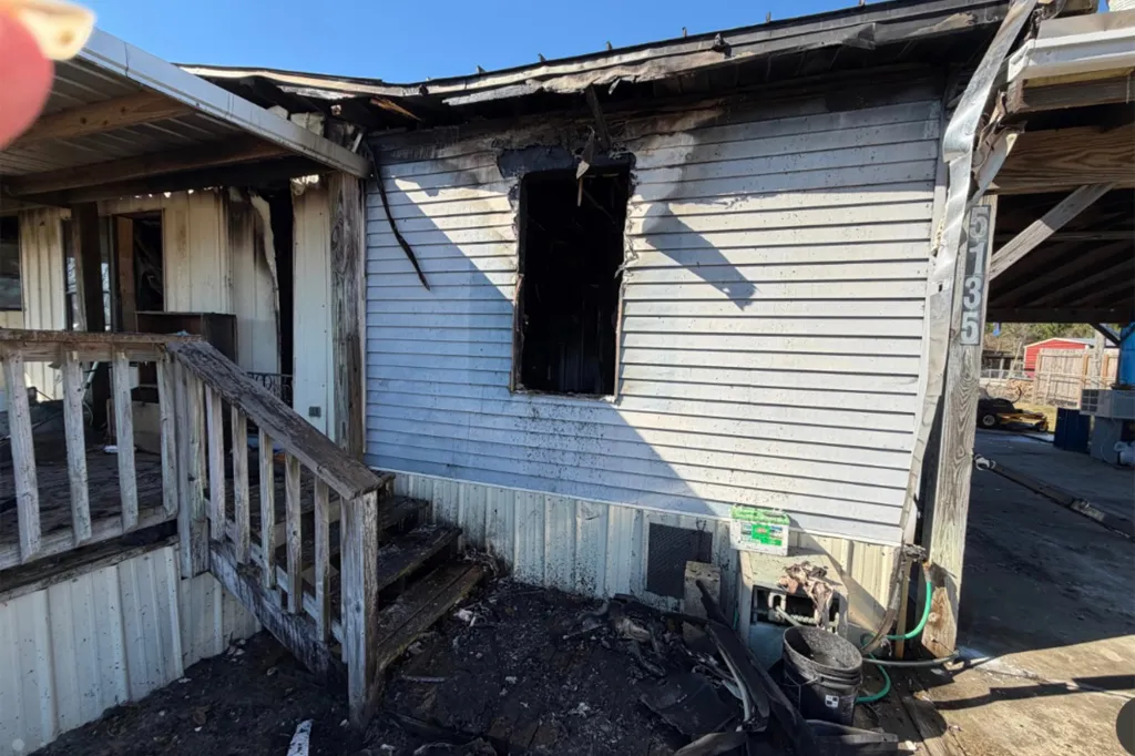 The exterior of a house partially destroyed by fire, with a collapsed roof and blackened walls.