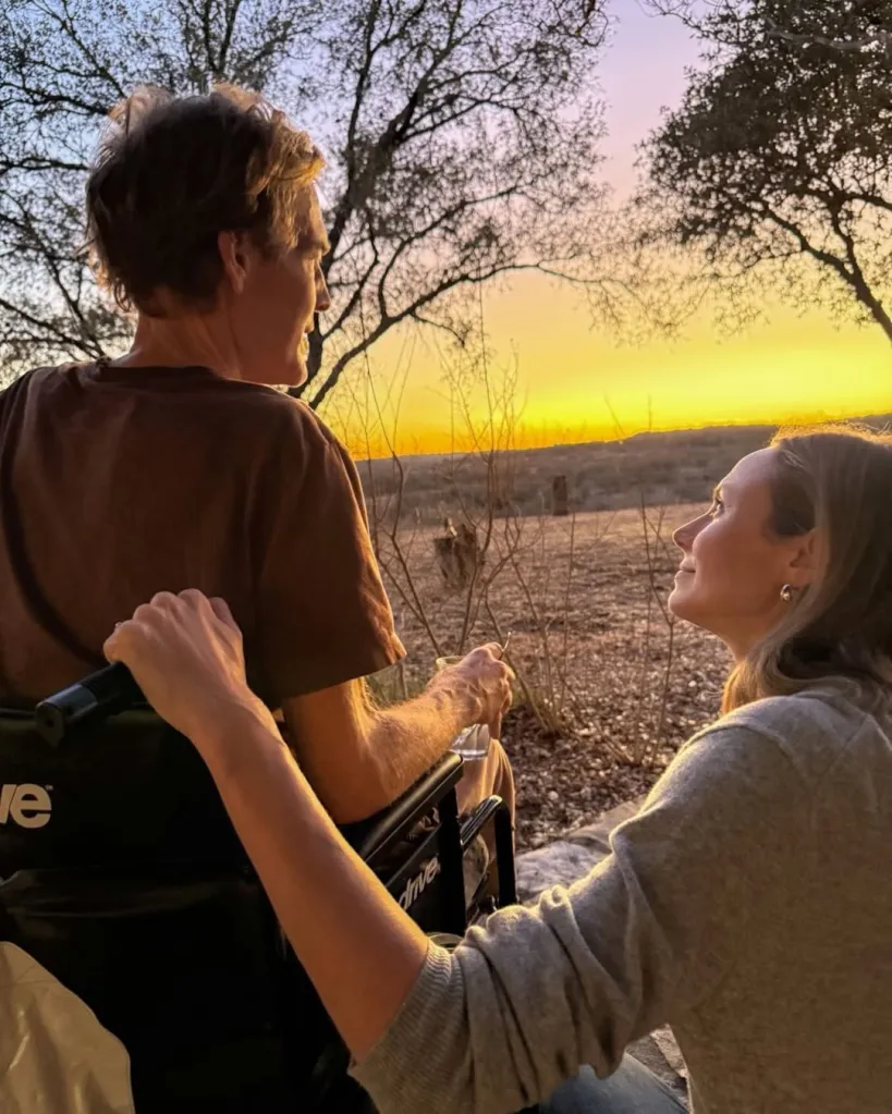 Stacy Keibler smiling at James Van Der Beek sitting in a wheelchair at sunset.