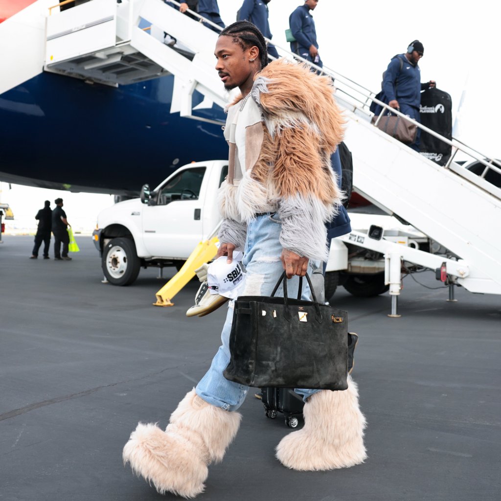 Stefon Diggs walking with a large Birkin bag and fur boots next to an airplane.