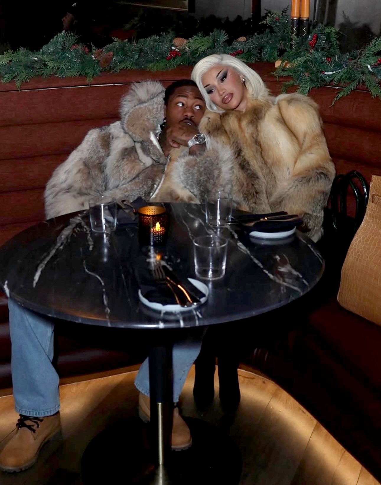 Stefon Diggs and Cardi B embracing at a table in a restaurant.