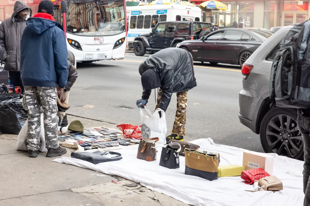 Street vendors selling counterfeit luxury brand bags, watches, and sunglasses along Canal Street and Broadway in Chinatown, Manhattan.