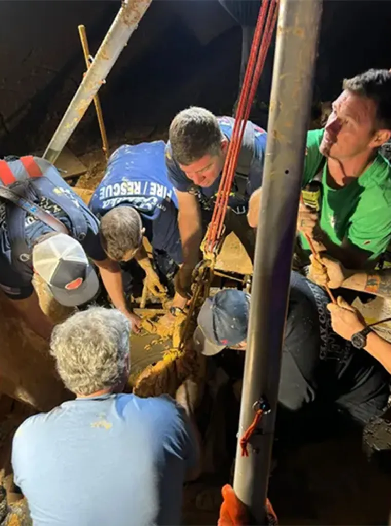 Rescuers working to free a person from deep mud at night.