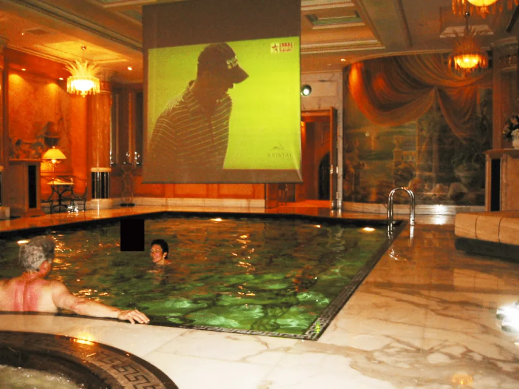 clinton and maxwell in pool with a large screen showing a golf game along with a third person whose face is redacted