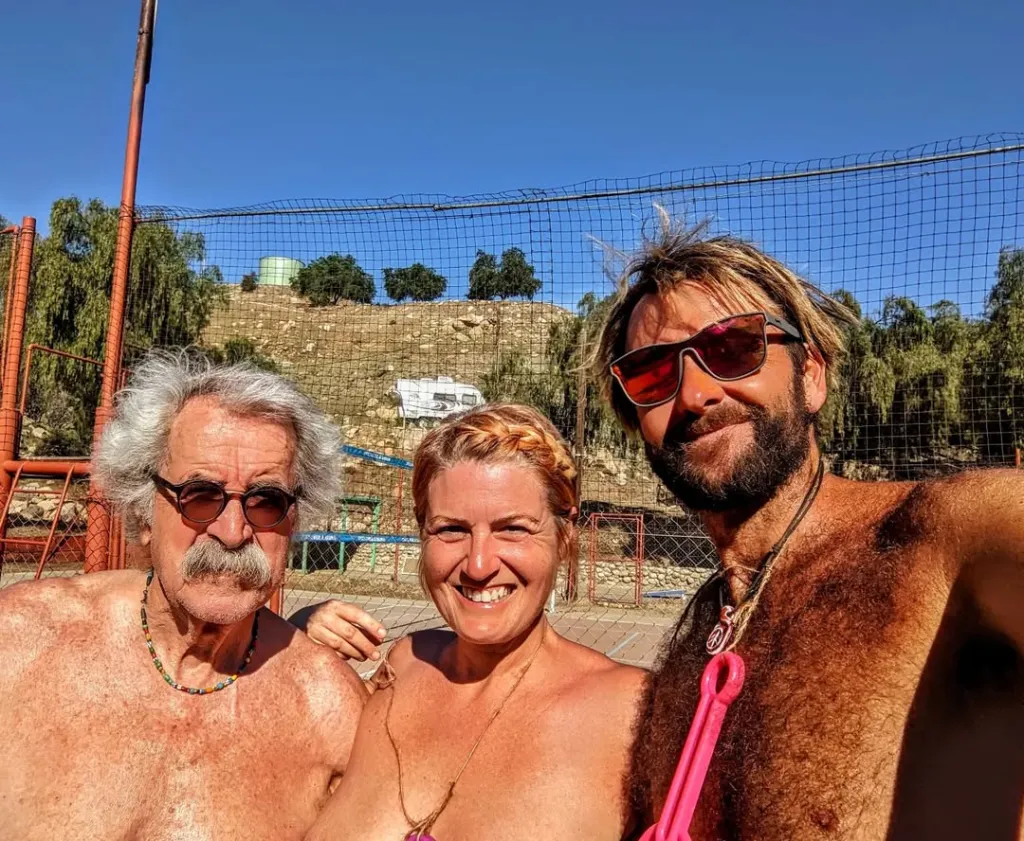 Three people, two men and one woman, smiling outside with a fence and hills in the background.