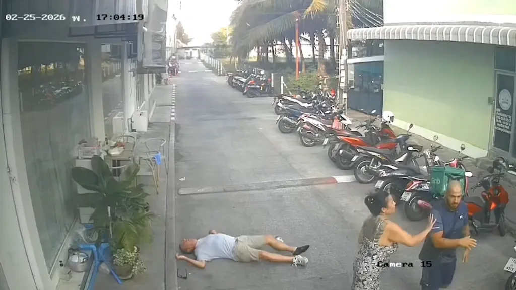 A man lies unconscious on the ground after being struck by another man, who is being restrained by a woman.