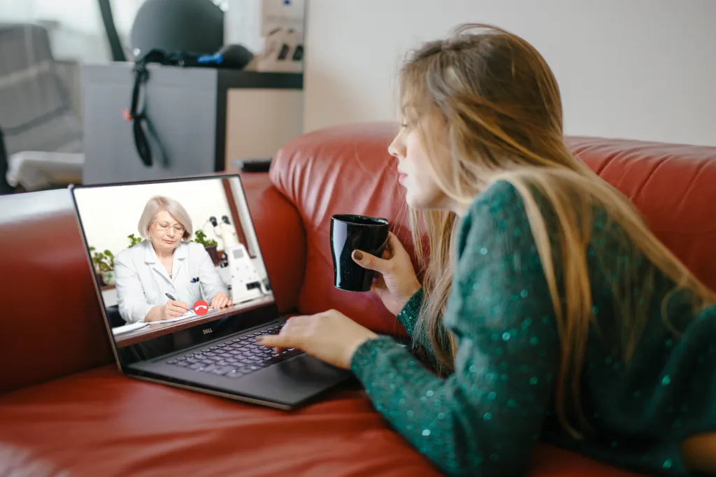 Woman on a red couch having a video consultation with a female doctor on her laptop.