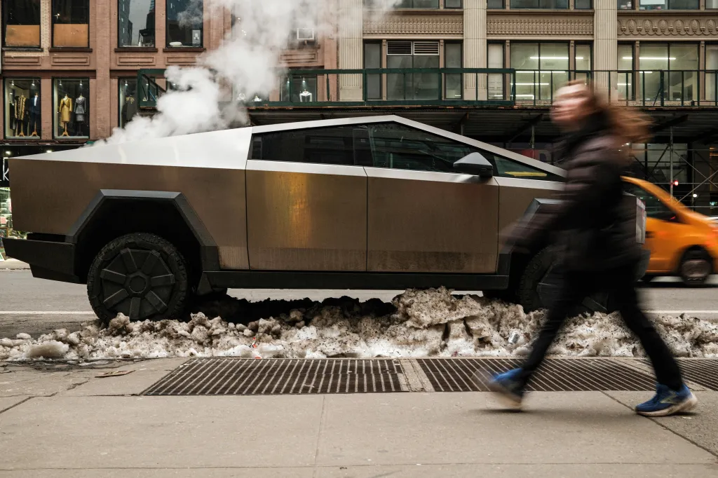 Tesla Cybertruck parked on a snow-lined street in Manhattan with a blurry person walking by.