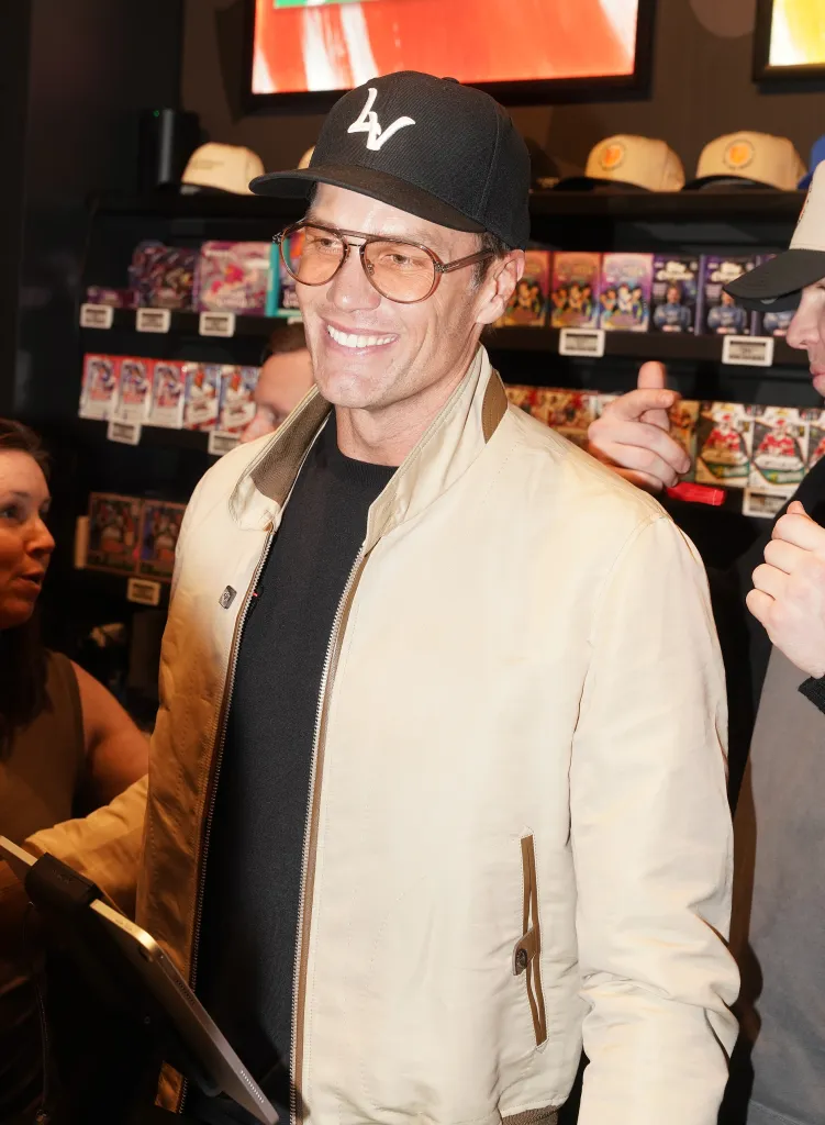 Tom Brady smiling while wearing a black baseball cap and brown-tinted glasses.