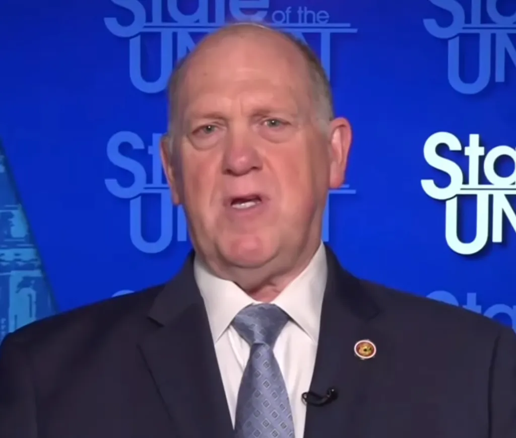 Tom Homan speaking against a blue background with 