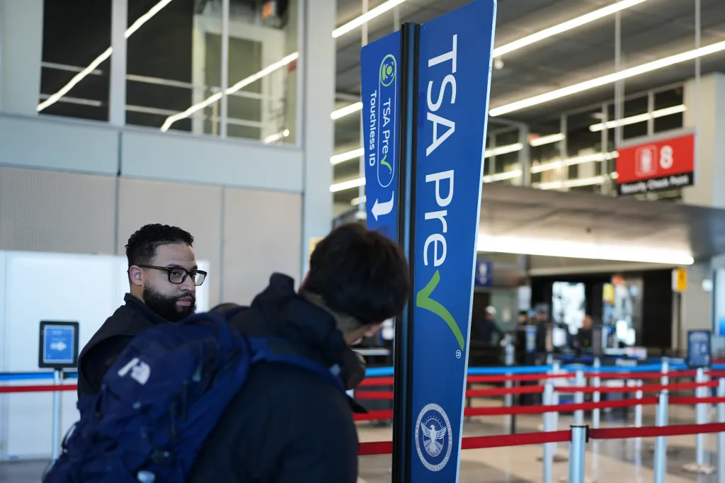 A man with a beard and glasses looking over his shoulder at the TSA Precheck line.
