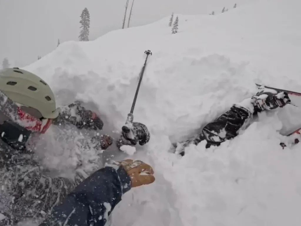 Three people caught in an avalanche are partially covered in snow, with a ski pole sticking out of the snow.