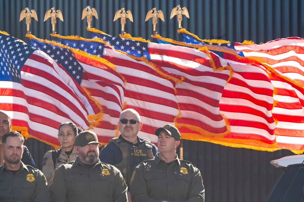 U.S. Department of Homeland Security agents at the U.S.-Mexico border near Nogales, Arizona, with American flags and golden eagle finials behind them.