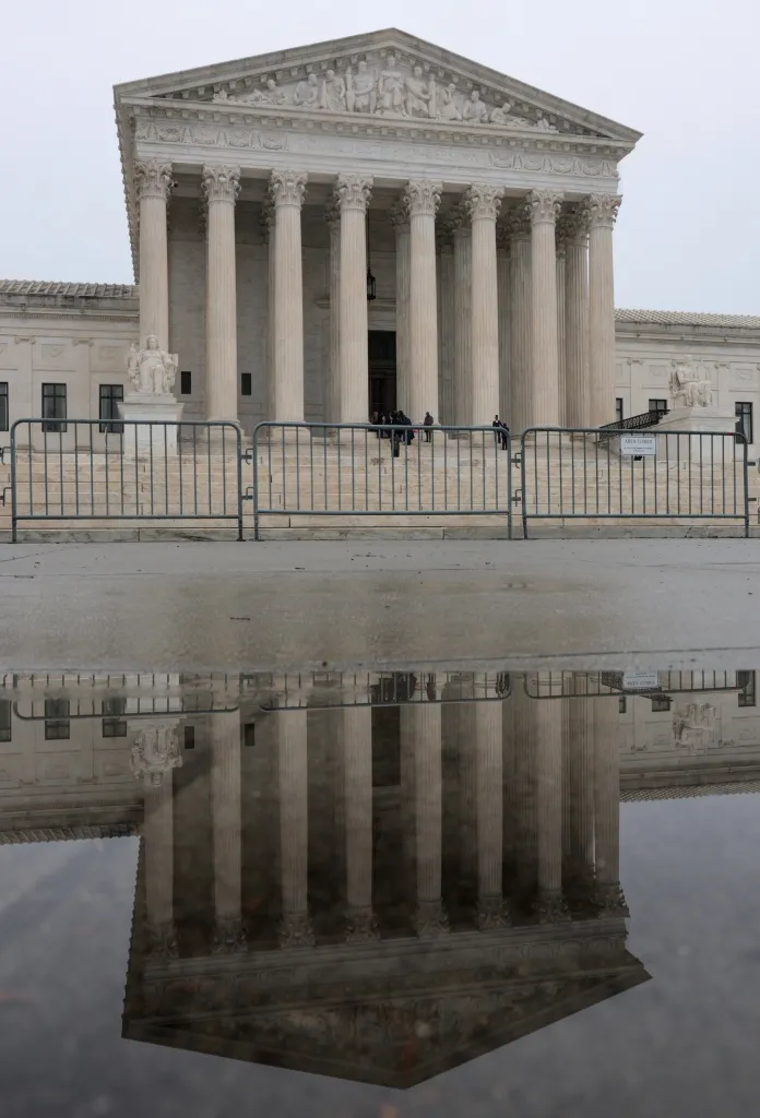 The U.S. Supreme Court building reflected in a puddle on a gray day.