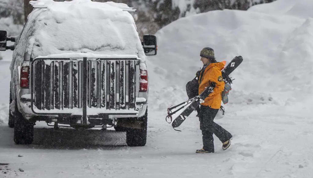 A member of the Nevada County Sheriff Search and Rescue team carries skis and a pack in the snow next to a snow-covered truck.