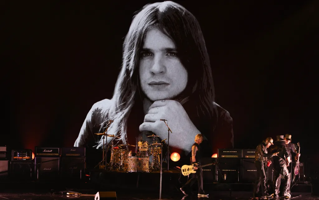 A black and white image of Ozzy Osbourne is displayed on a large screen during a live musical performance.