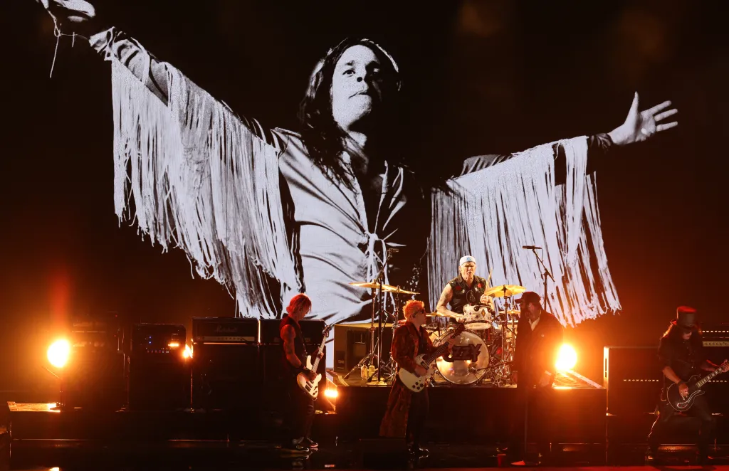 Musicians Duff McKagan, Andrew Watt, Chad Smith, Post Malone, and Slash perform onstage with a black and white image of Ozzy Osbourne in the background.