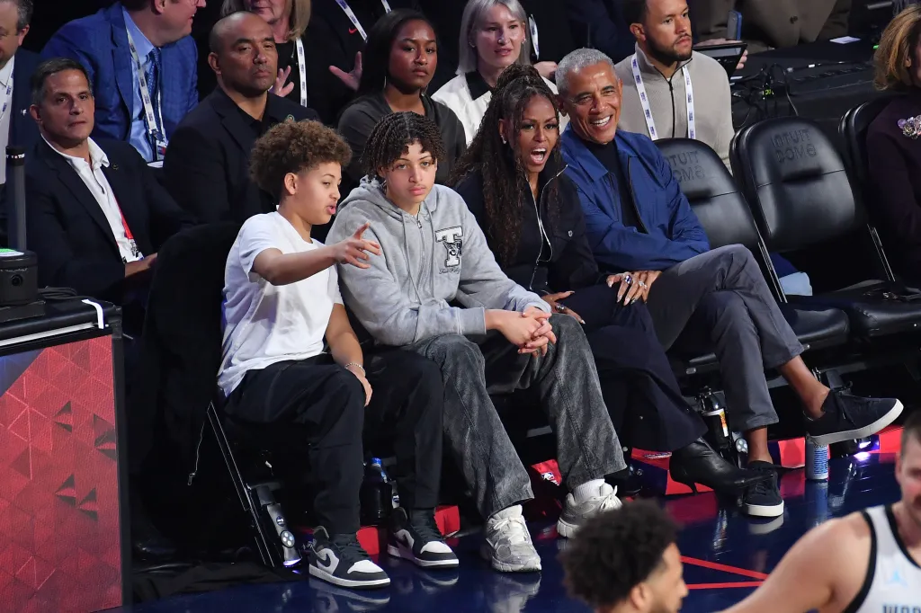 Barack and Michelle Obama with two young men and other spectators watching an NBA game.