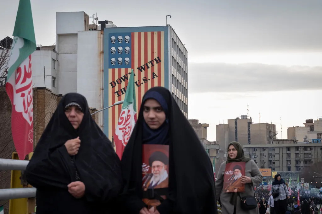 Veiled Iranian women carry portraits of Ayatollah Ali Khamenei and walk under an anti-U.S. mural.