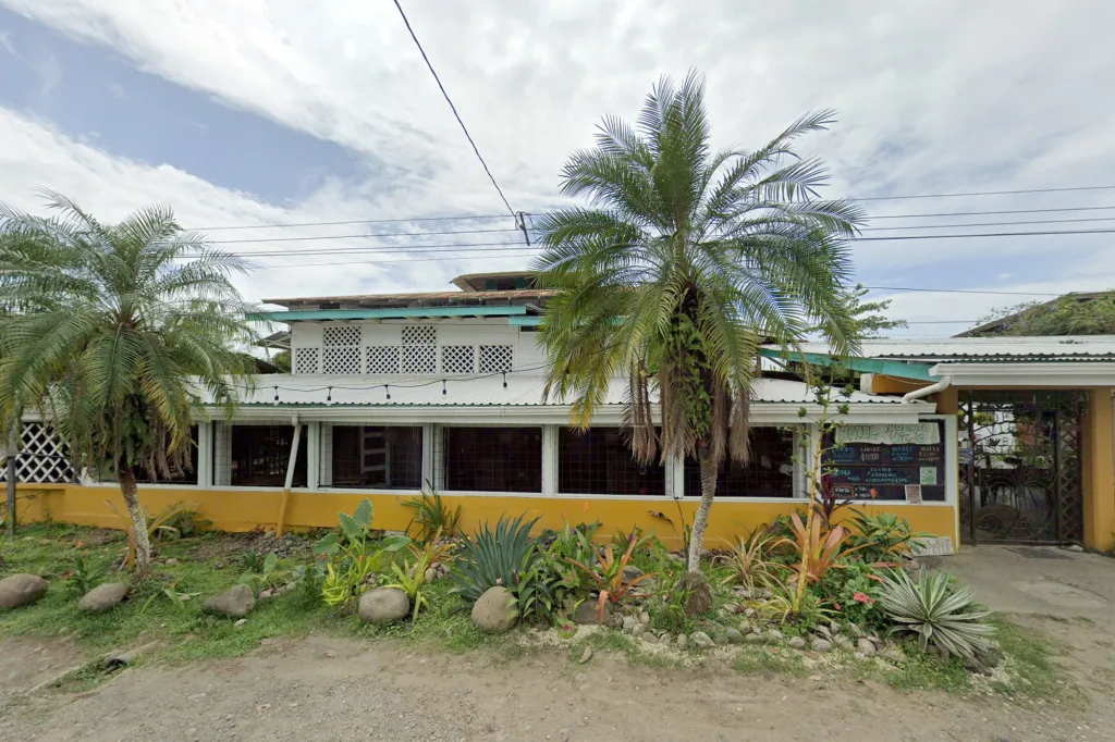 The Hotel Puerto Viejo with its yellow and white facade, surrounded by palm trees and tropical plants.