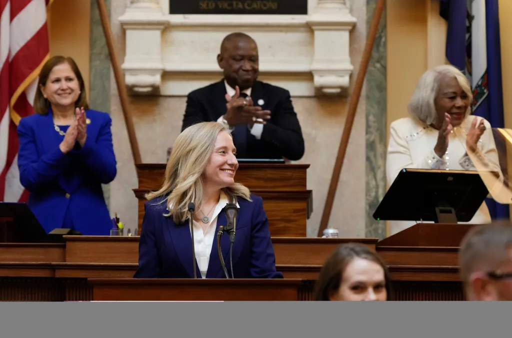 Abigail Spanberger smiles at the podium while three people applaud her.