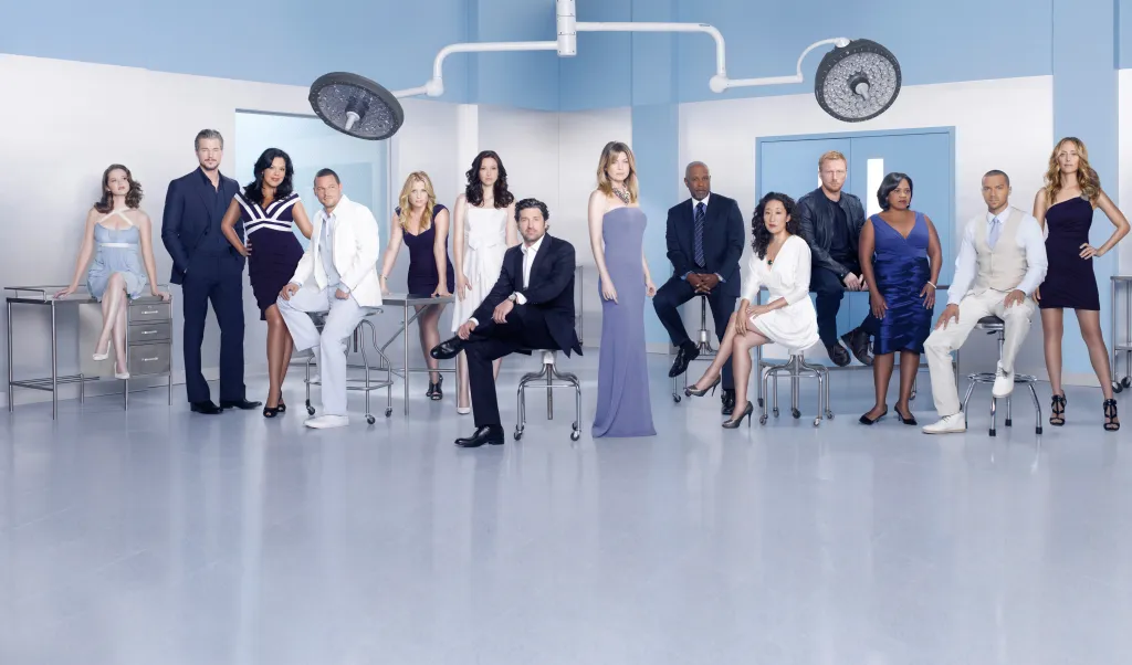The cast of Grey's Anatomy poses in a light blue room with medical equipment.