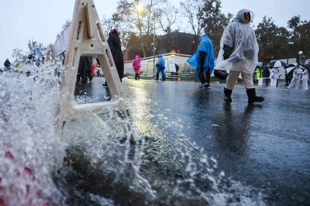 Rainwater splashes on Colorado Blvd as parade attendees wearing ponchos walk before the Rose Parade.