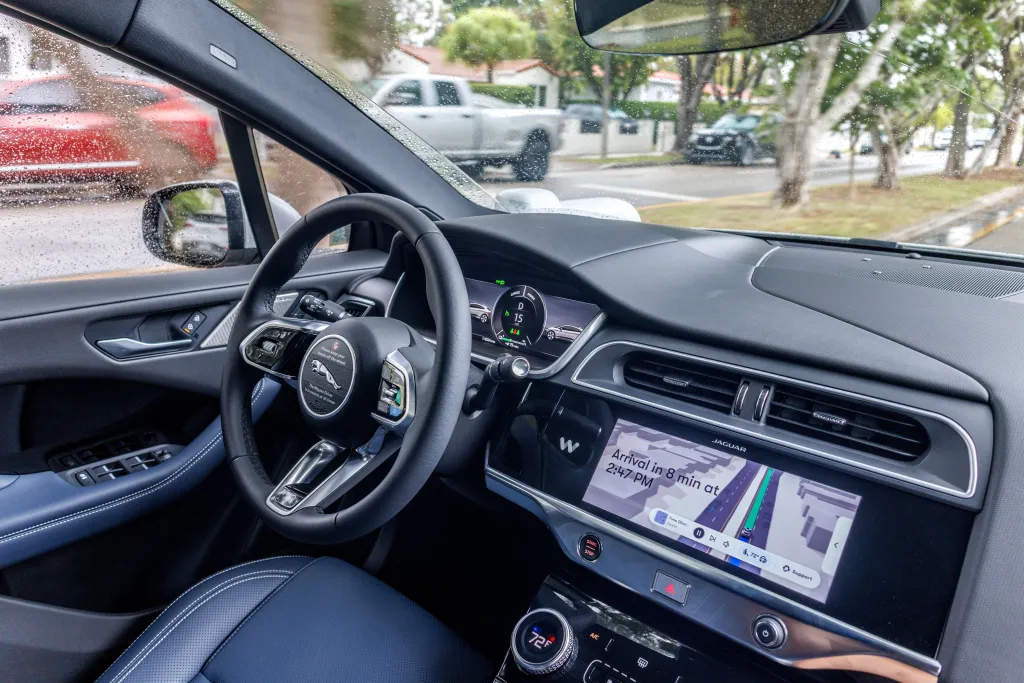 Interior of a Waymo self-driving car showing the steering wheel, dashboard, and navigation screen.