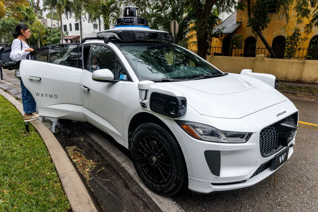 A woman exiting a white Waymo autonomous car.
