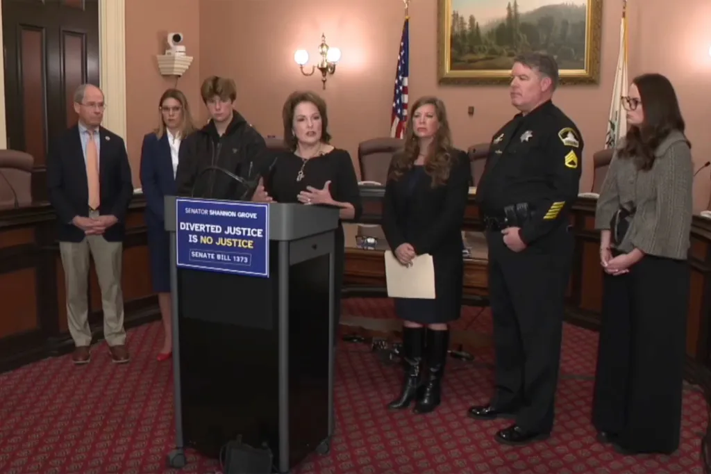A group of people, including the wife and son of former Kern County Supervisor Zack Scrivner, speak at a podium with a sign that reads 