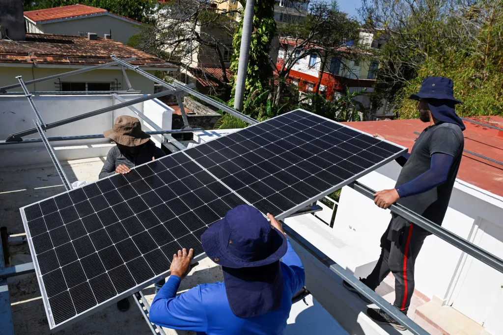 Three workers installing a solar panel on a rooftop in Havana, Cuba.