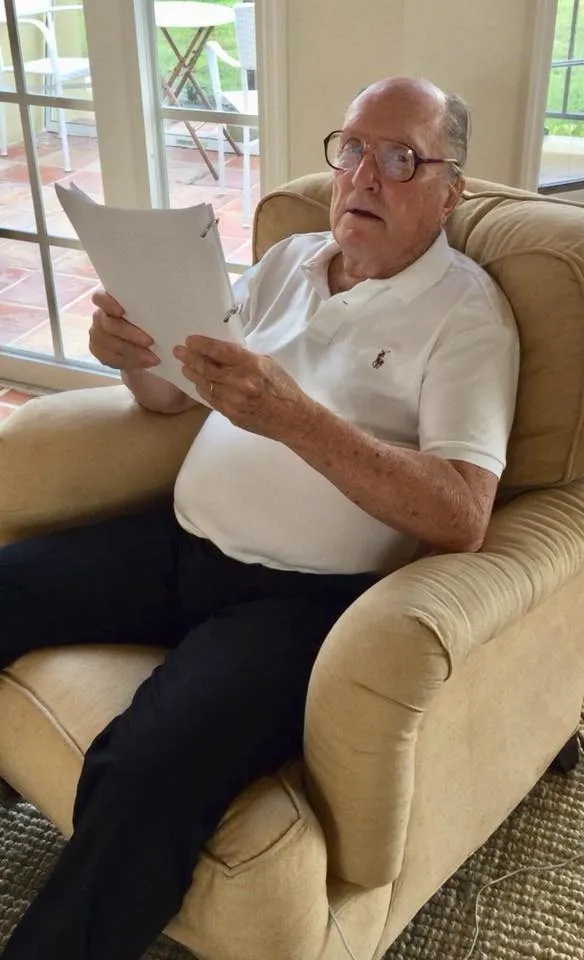 Robert Duvall reading a script while sitting in a cream-colored armchair.