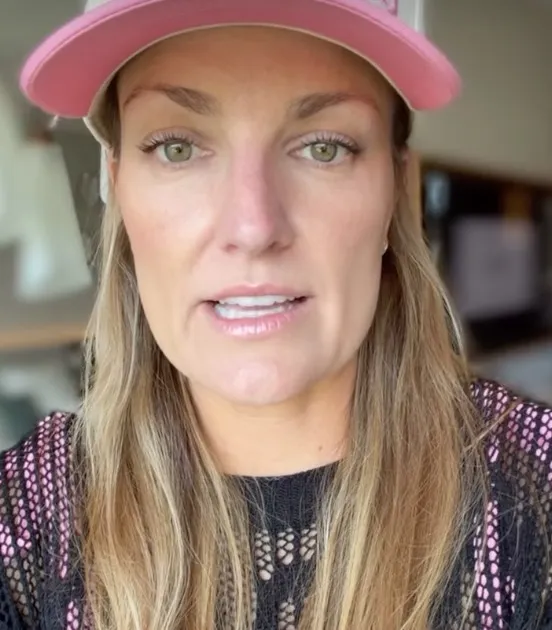 Katy Holloman, a woman with long blonde hair and a pink visor, speaking to the camera.