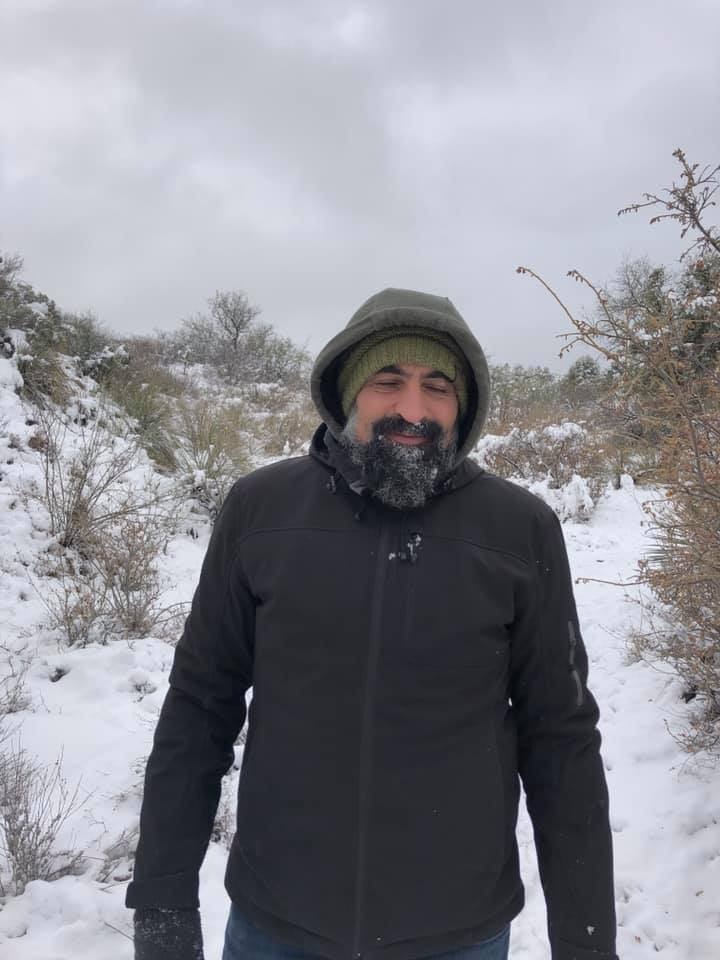 Tommaso Cioni standing in the snow with snow on his beard and in his hooded jacket.